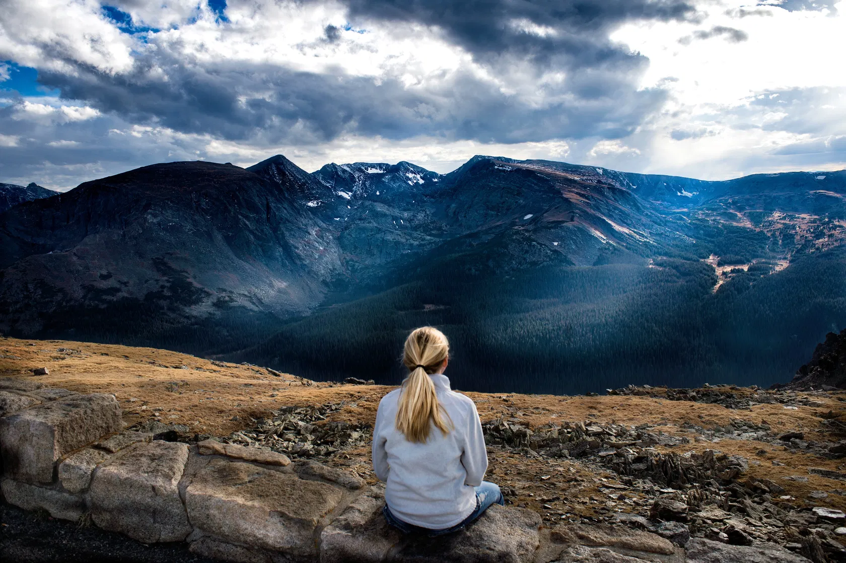 Frau sitzt auf dem Berg, bedeckter Himmel mit Bergaussicht