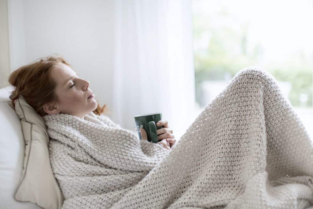 Woman with a cold under the blanket with a cup of tea