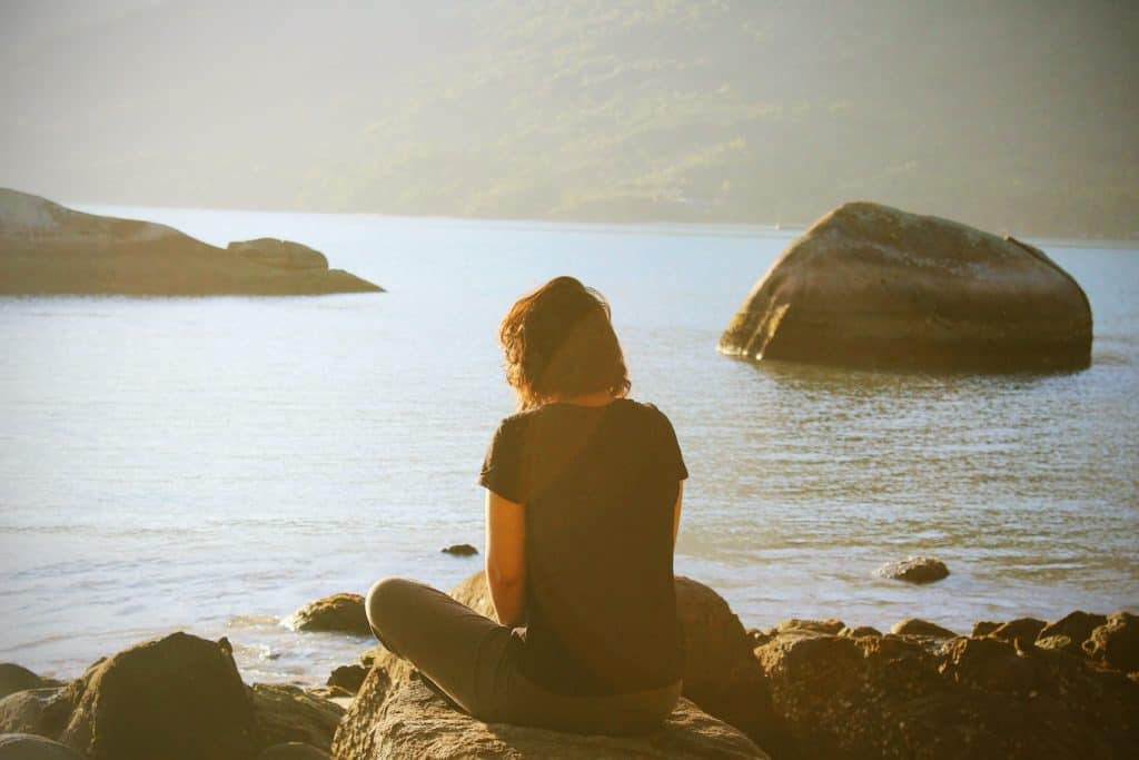 Woman sitting by a body of water and meditating