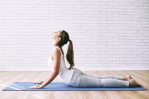 Eine Frau in Sportkleidung führt die Yoga-Übung Kobra aus. Sie liegt auf dem Boden und hebt den Oberkörper.