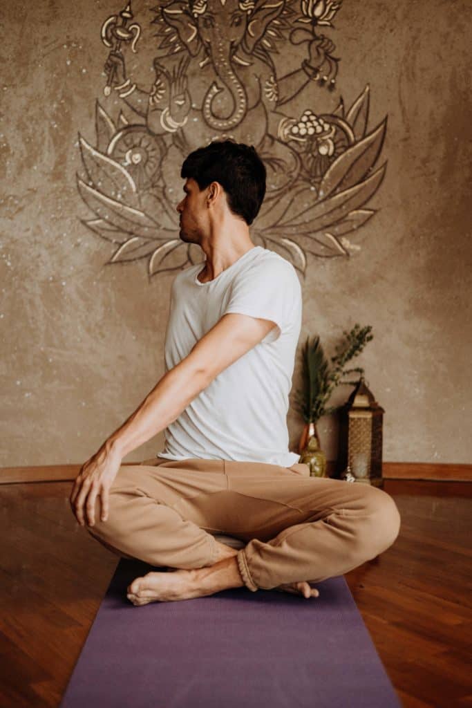 A man sits with his legs crossed on a yoga mat and his upper body turned backwards