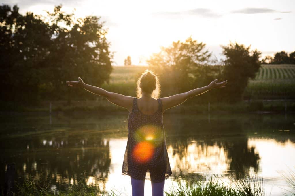 A woman stands by a lake and spreads her arms to feel the energy of the portal days.