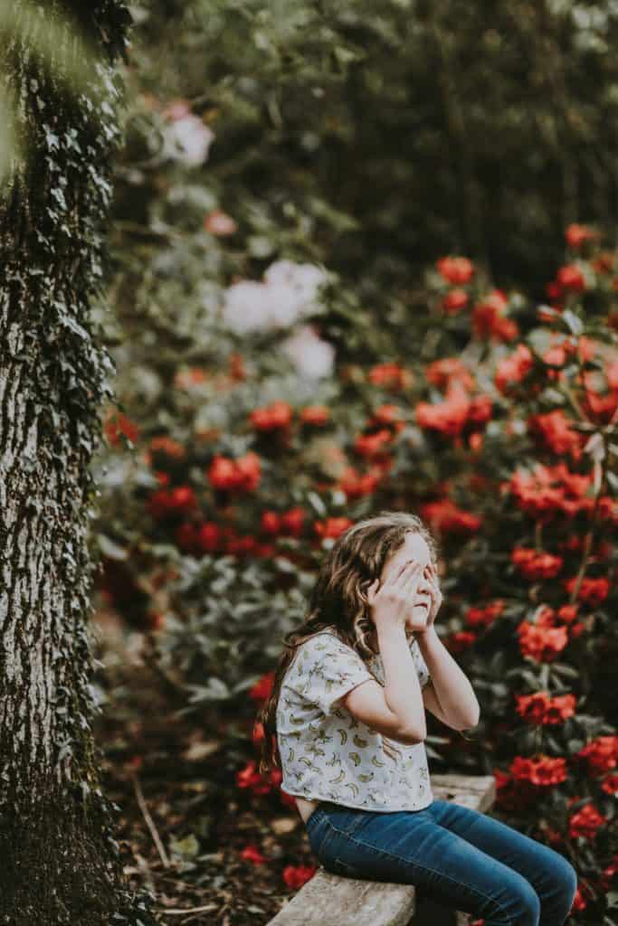 Ein Kind, das auf einem Baumstamm sitzt und verzweifelt die Hände vor das Gesicht schlägt. Als Metapher für Dein inneres Kind. 