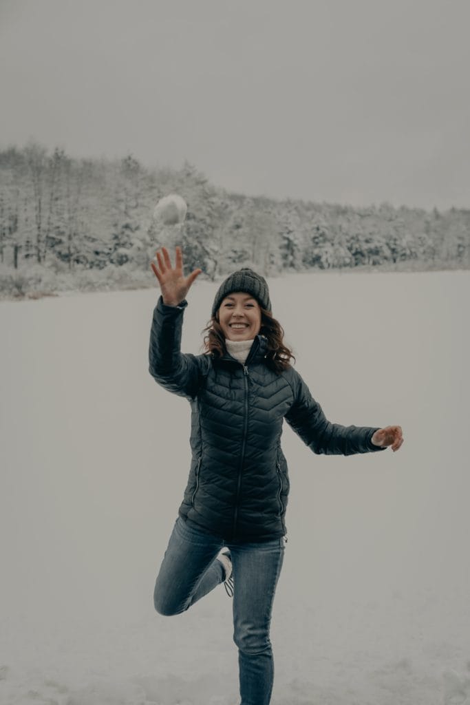 Eine Frau in einer Schneelandschaft, die einen Schneeball fängt. Spiel und Spaß unterstützt Dein inneres Kind. 
